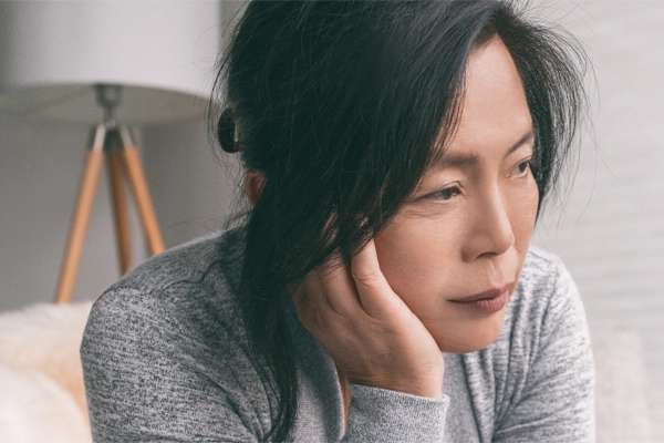 Adrenal-Fatigue-Doctor A middle-aged asian woman sitting on her couch, resting her head on her hand, suffering from adrenal fatigue. Get treatment for adrenal fatigue syndrome from Tanya Zboril, NP of TBT Medical in Kitchener-Waterloo.