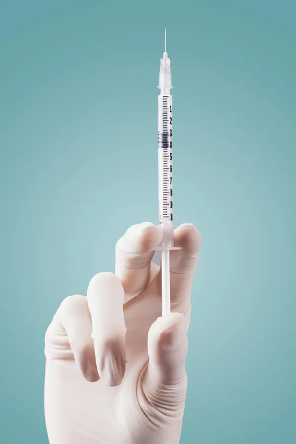Aesthetic-Fillers-Treatment Close-up of a white-gloved hand holding a syringe against a light blue background, representing aesthetic filler services from Tanya Zboril, NP of TBT Medical in Kitchener-Waterloo.