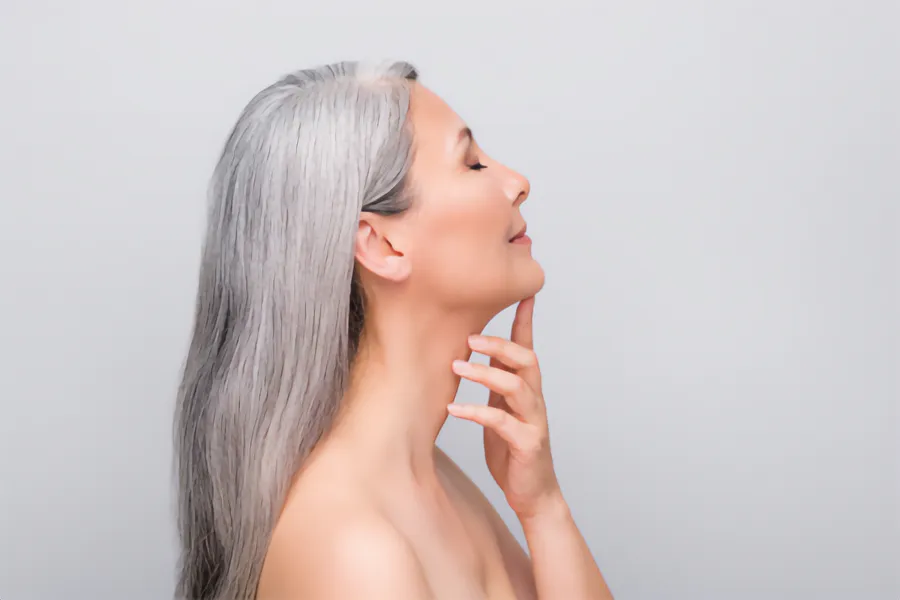Chin-Fat-Reduction-Clinic A mature asian woman seen in profile touching her well-shaped chin. Schedule chin fat reduction treatment from Tanya Zboril, NP of TBT Medical in Kitchener-Waterloo.