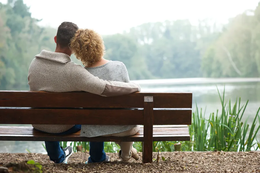 Functional-Medicine-Doctor A couple wearing sweaters seen from behind sitting on a bench and looking out at a relaxing lake and forest, representing functional medicine treatment from Tanya Zboril, NP of TBT Medical in Kitchener-Waterloo.
