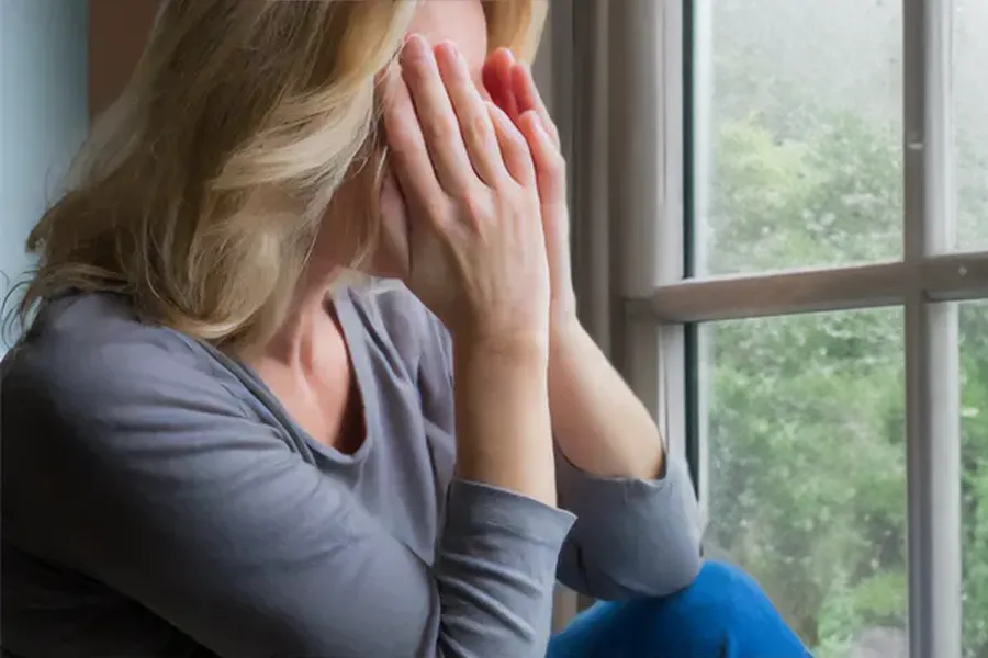 Graves-Disease-Clinic A blonde woman in a gray shirt sits in front of a window on a rainy day covering her eyes with her hands. Get treatment for Grave's Disease from Tanya Zboril, NP of TBT Medical in Kitchener-Waterloo.