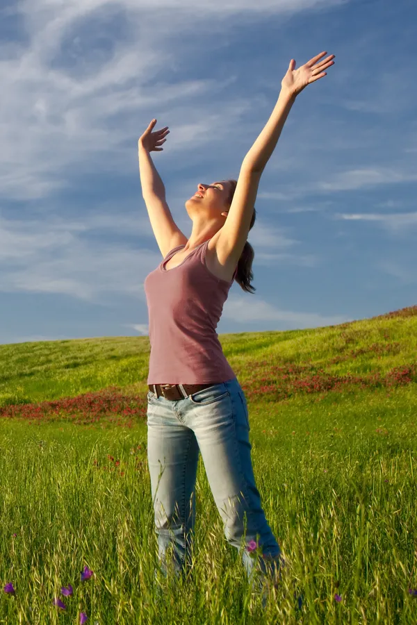 Graves-Disease-Treatment A woman in a tank top and jeans looks up with her arms outstretched to the sky in a field after successful treatment for Grave's Disease from Tanya Zboril, NP of TBT Medical in Kitchener-Waterloo.