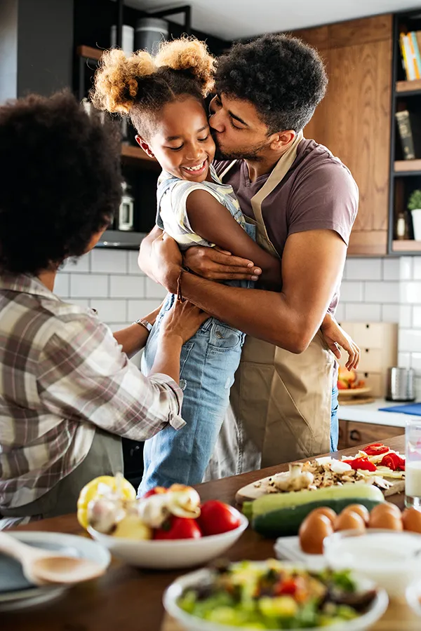 Gut-Health-Treatment A man holds his daughter and kisses her cheek as the family makes a healthy dinner in the kitchen. Get help for digestive issues and gut health from Tanya Zboril, NP of TBT Medical in Kitchener-Waterloo.