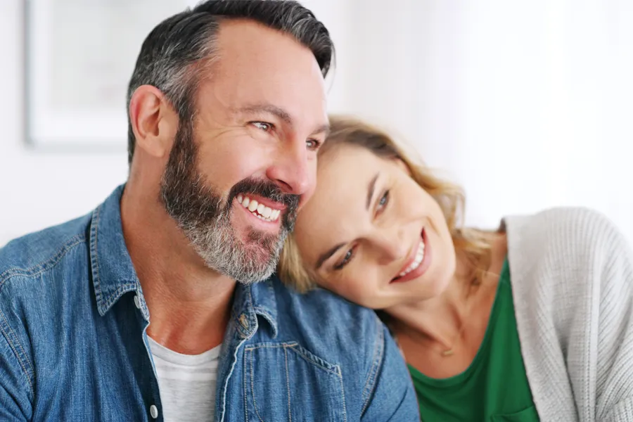 A middle-aged white couple in a bright white room smile and lay their heads on each other. Schedule concierge health and wellness services from Tanya Zboril, NP of TBT Medical in Kitchener-Waterloo.