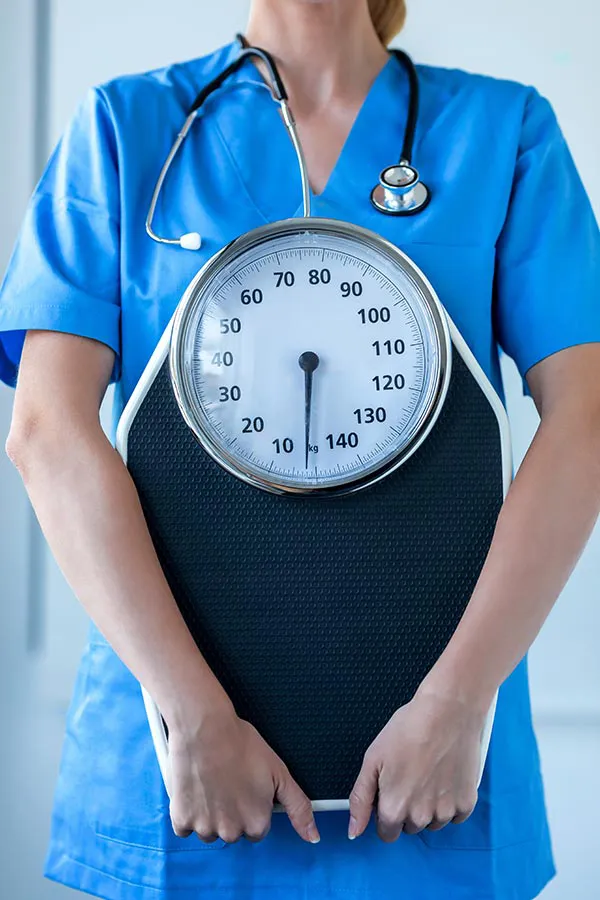 Medical-Weight-Loss-Treatment A nurse in blue scrubs with a stethoscope hanging around her neck holds a scale, representing weight loss treatments from Tanya Zboril, NP of TBT Medical in Kitchener-Waterloo.