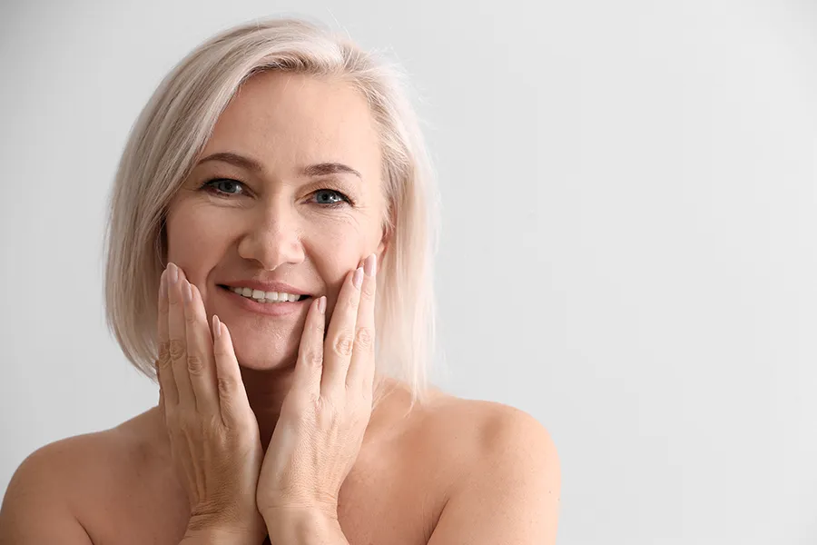 PRP-Microneedling-Clinic A mature woman touches her faces to feel the successful results of PRP microneedling and skin rejuvenation treatments from Tanya Zboril, NP of TBT Medical in Kitchener-Waterloo.