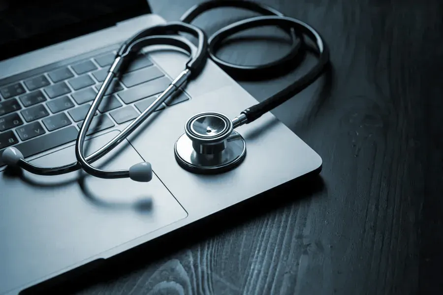 Telemedicine-Doctor An open laptop with a stethoscope lying on it on a wooden table, symbolizing telemedicine care from Tanya Zboril, NP of TBT Medical in Kitchener-Waterloo.